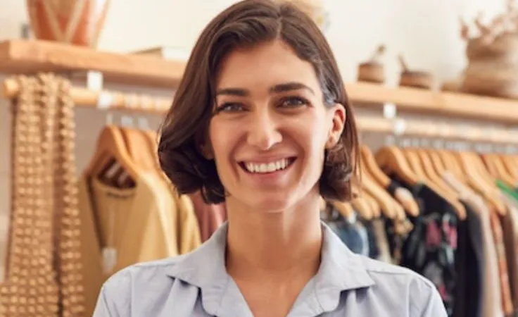 A shop assistant smiling with a tablet in front of clothing rails in a store